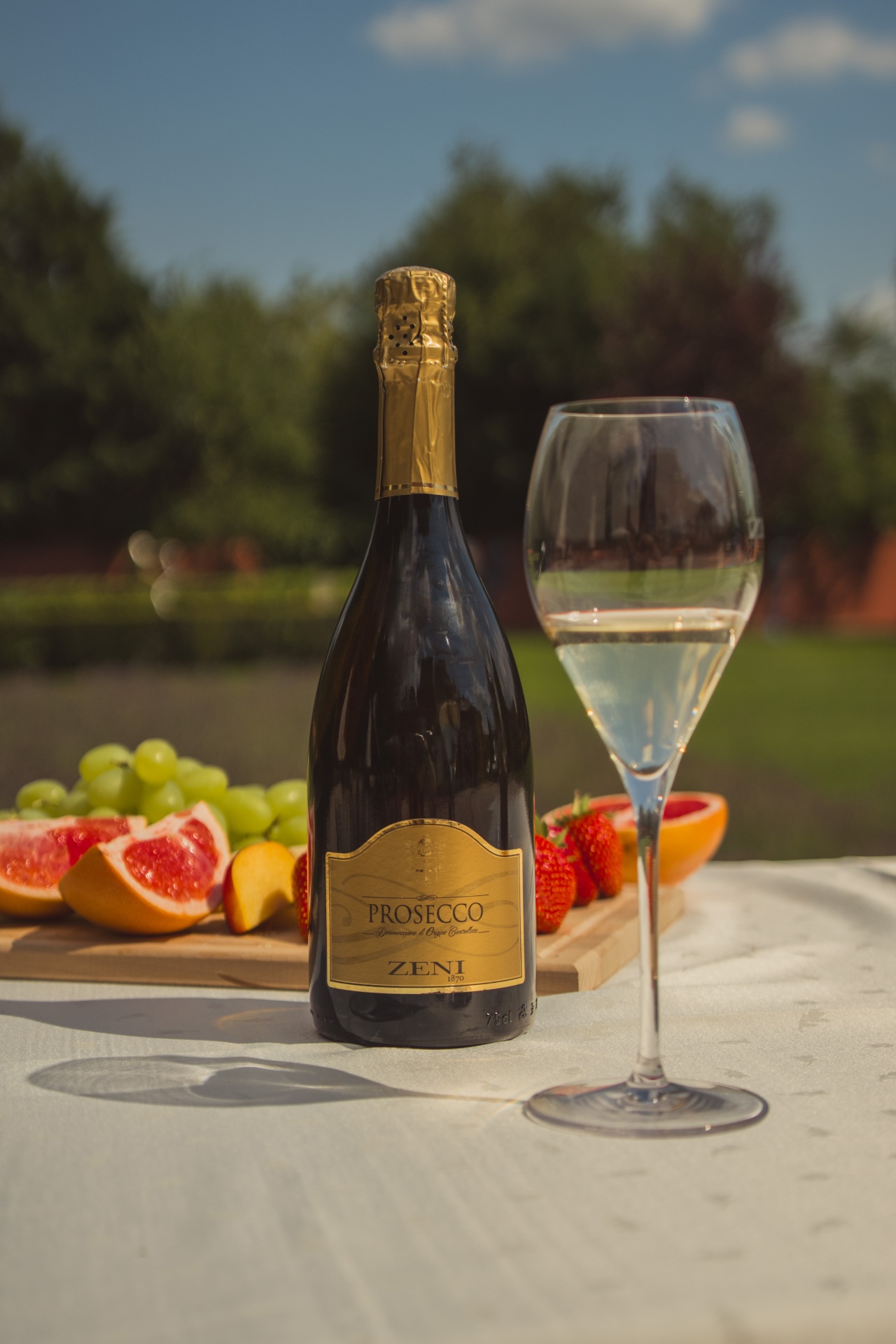 Zeni 1870 Prosecco palack pohárral és friss gyümölcsökkel a szabadban